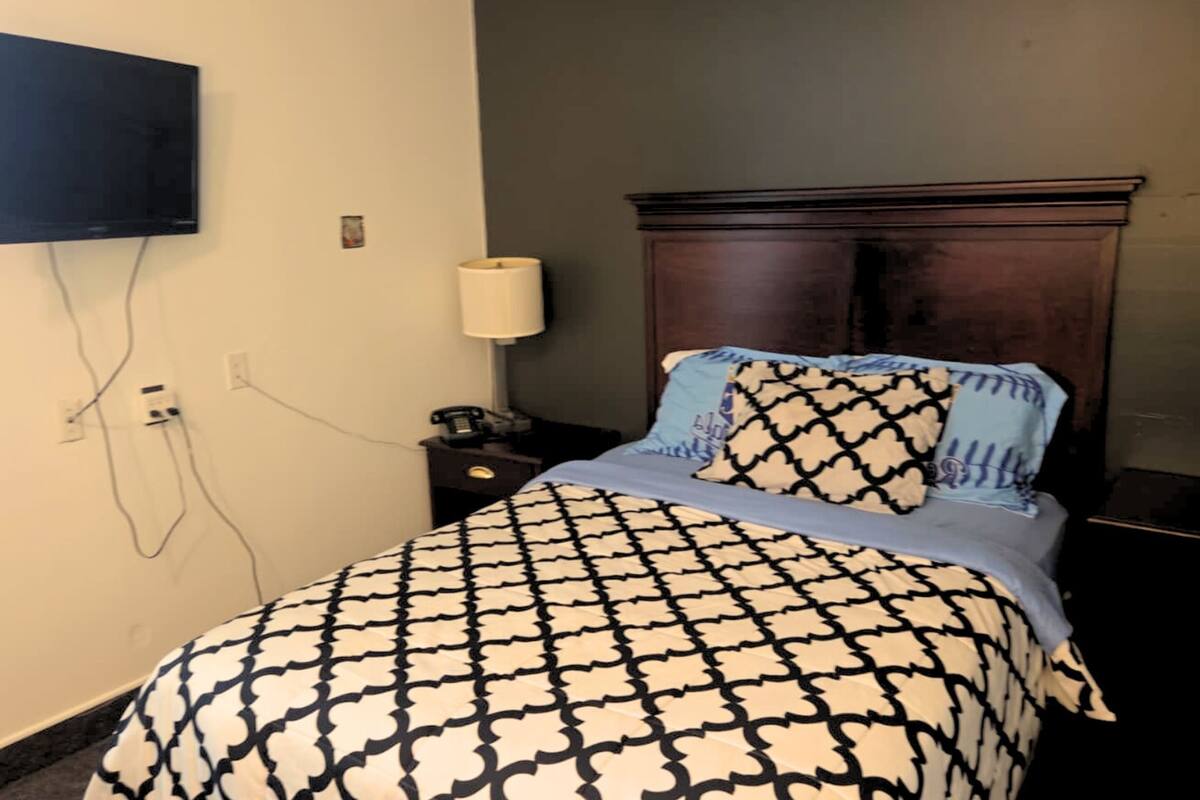 A hotel room with a bed, a nightstand, a lamp, and a TV mounted on the wall.