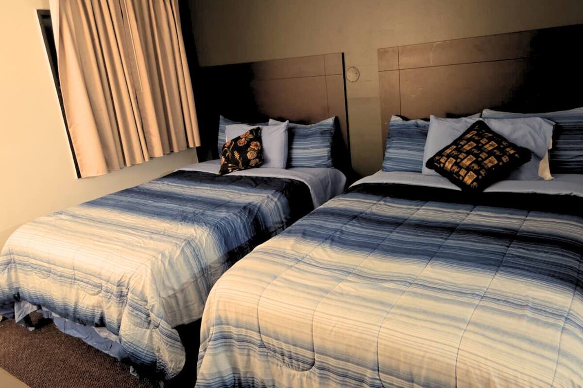 A hotel room with two beds, each with a striped bedspread and matching pillows.