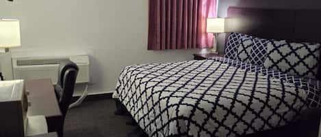A hotel room with a bed, a desk, a chair, a lamp, and a window with curtains.