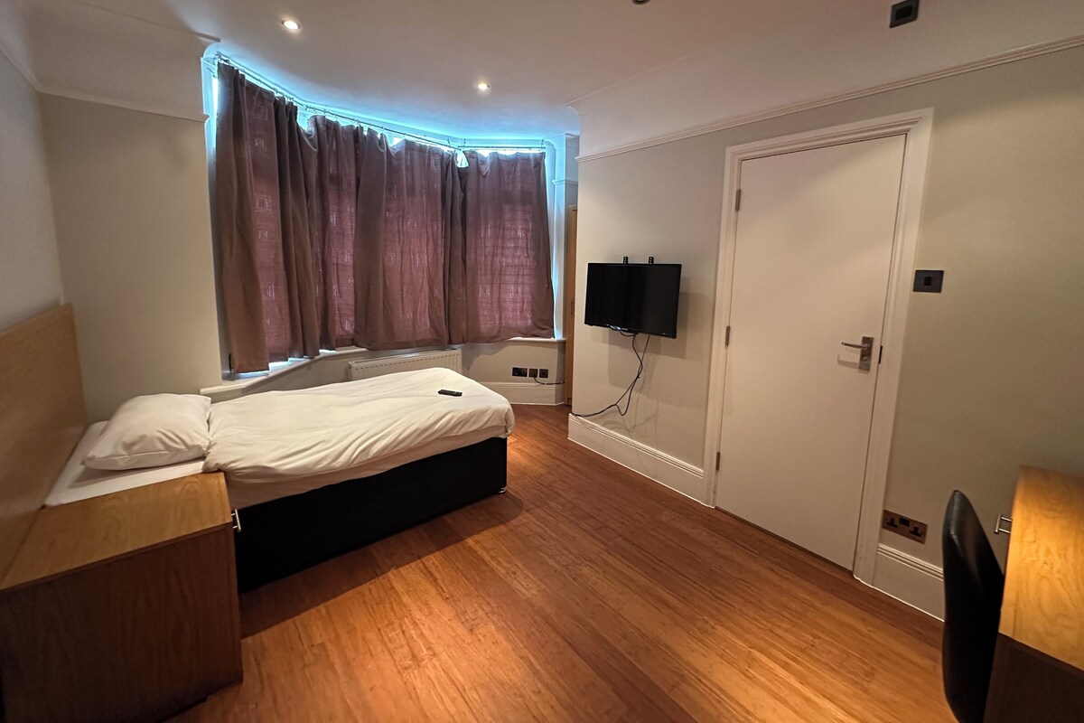 Ein Hotelzimmer mit Bett, Wandfernseher, Tür und einem fensterbepflanzten Fenster.