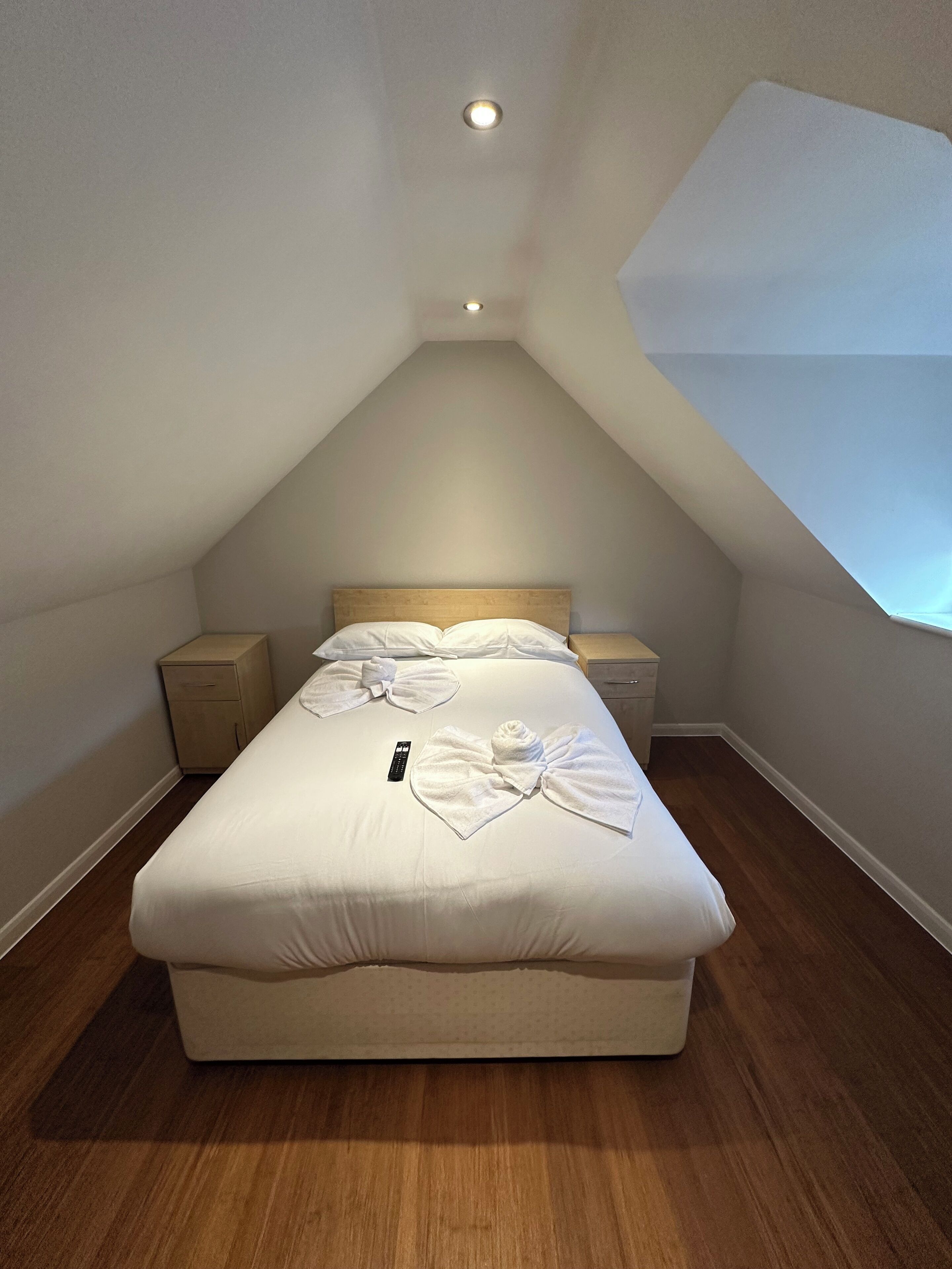 A bedroom with a single bed, a nightstand, a bedside table, and a remote control on the bed.