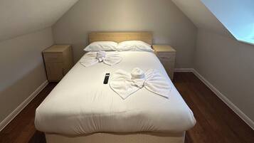 A bedroom with a single bed, a nightstand, a bedside table, and a remote control on the bed.