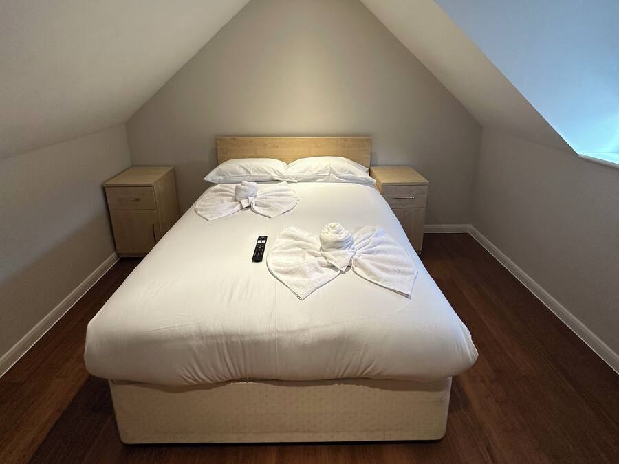 A bedroom with a single bed, a nightstand, a bedside table, and a remote control on the bed.