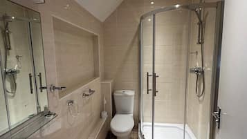 Un baño moderno con ducha envuelta en vidrio, inodoro blanco y lavabo con espejo superior.