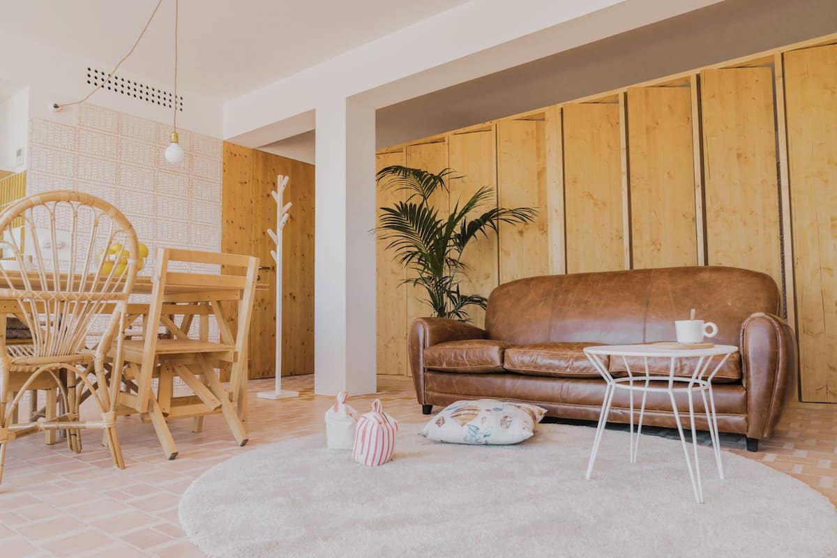 Una sala de estar acogedora con un sofá de cuero marrón, una mesita de café blanca, un sillón de mimbre y una planta en maceta.