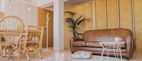 Een gezellige woonkamer met een bruine leren bank, een witte salontafel, een rieten fauteuil en een potplant.