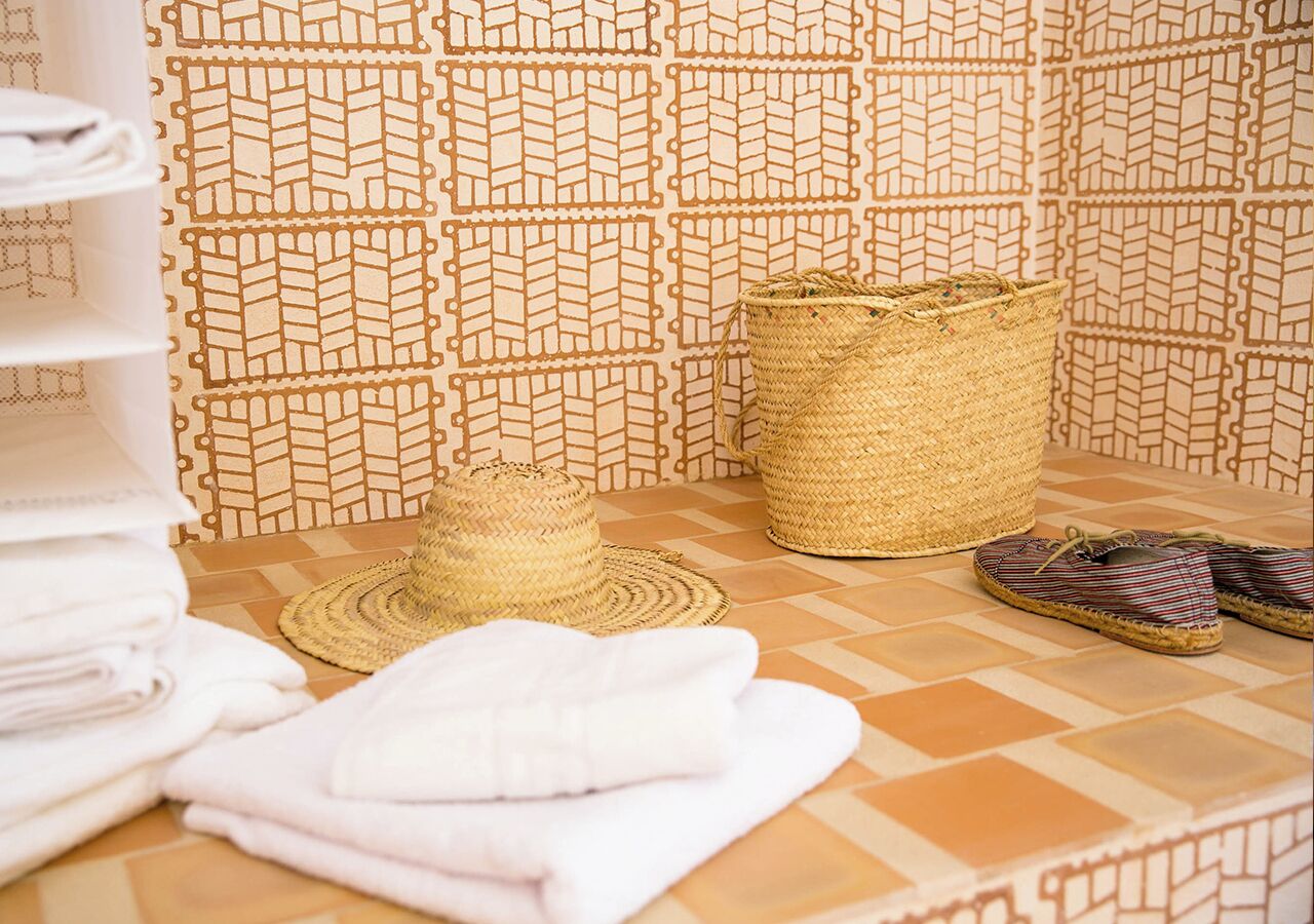A bathroom with a patterned tile backsplash, a woven basket, folded towels, and a straw hat.