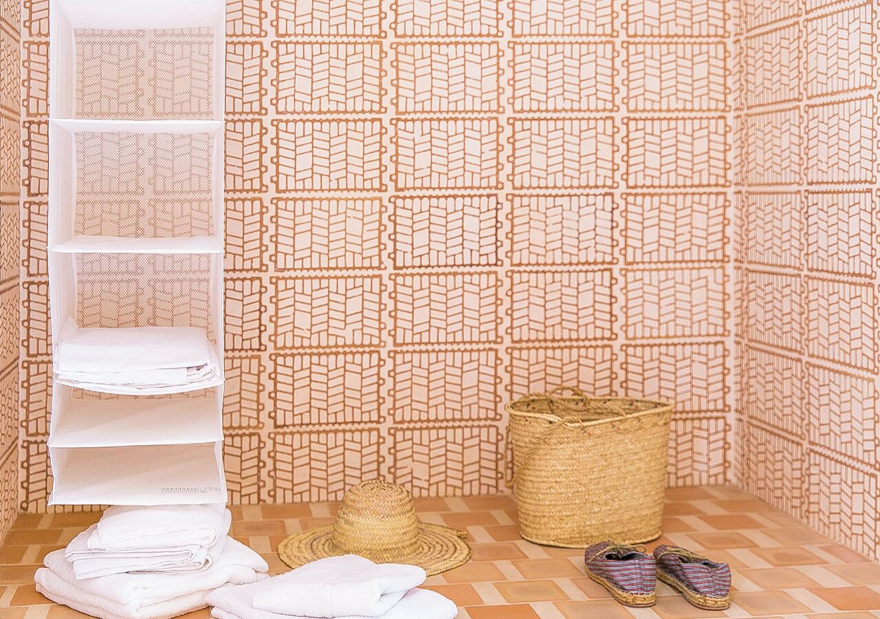 Een badkamer met een behang, een witte plank, een geweven mand en een paar schoenen.