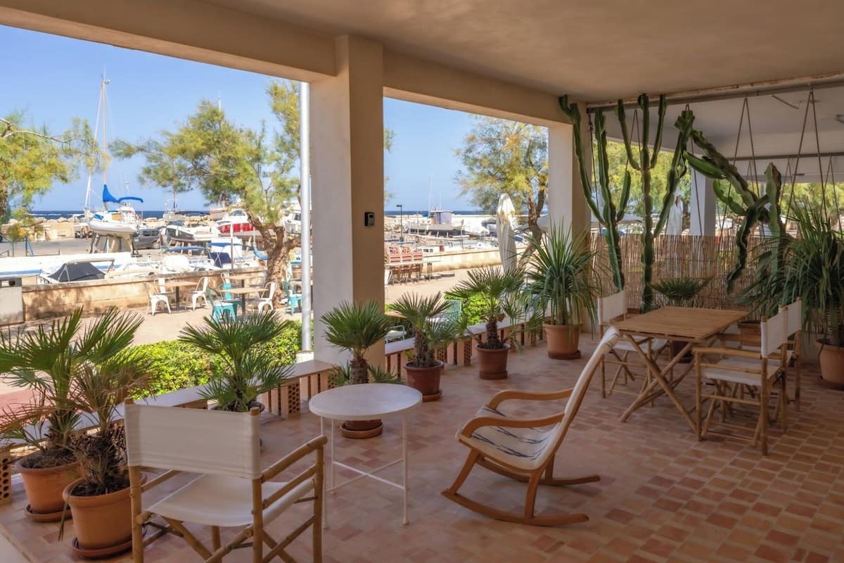 Un espacio de estar al aire libre cubierto con plantas en macetas, muebles de madera y vistas a barcos y árboles.
