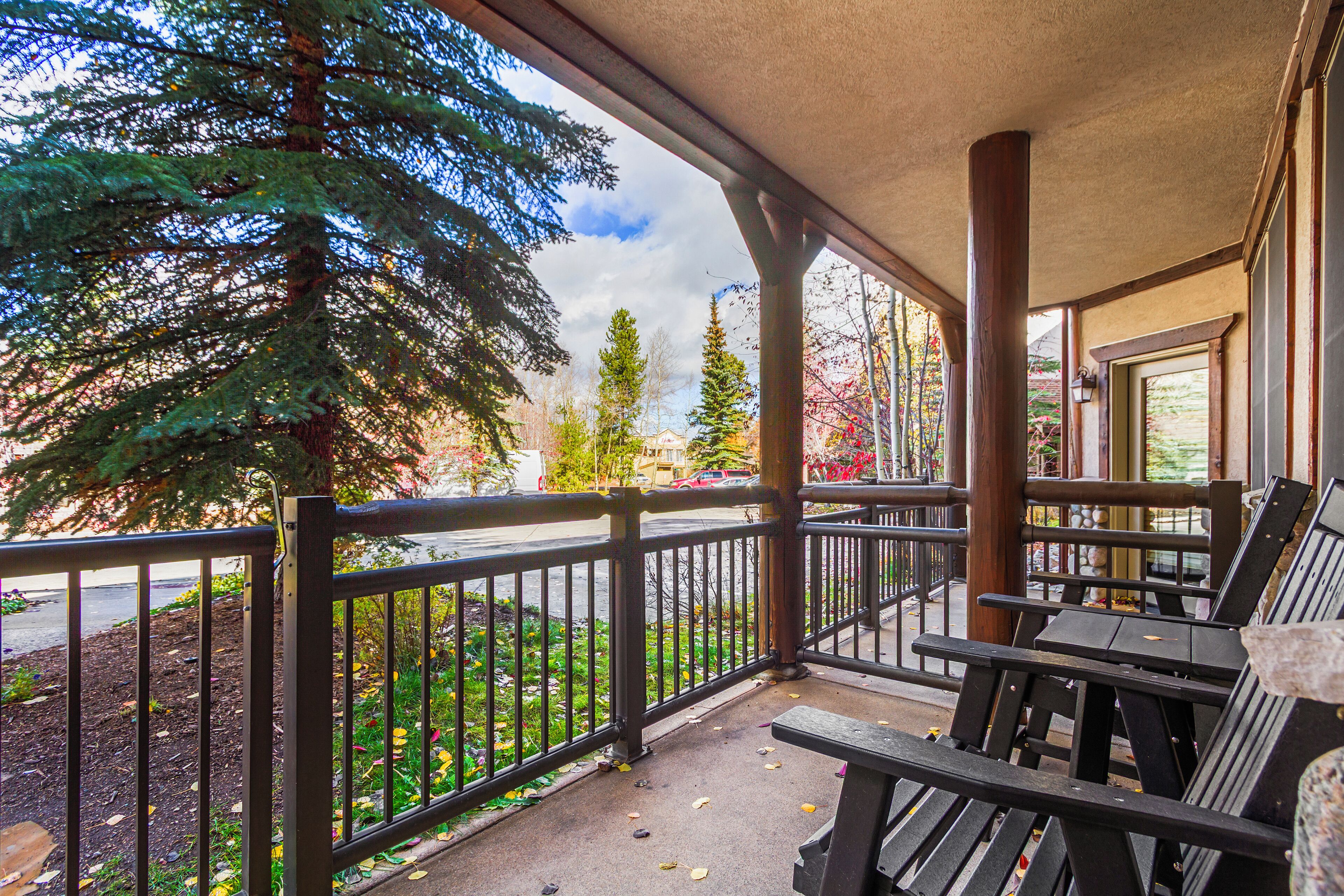 A porch with wooden railings, a bench, and a view of a street with trees and a building in the background.