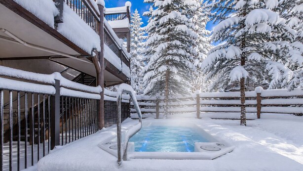 A snow-covered outdoor hot tub area with a wooden fence and snow-laden trees in the background.