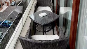Un balcón con mobiliario de mimbre, una lámpara decorativa y vistas a un paisaje urbano.