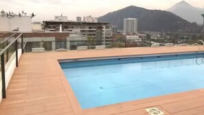 Una piscina en la azotea con vistas a una montaña y edificios al fondo.