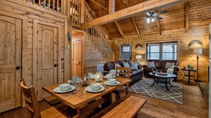 A wooden cabin interior with a dining area, a staircase, a sofa, and a ceiling fan. - 8 Miles to Pigeon Forge, 15 Miles to Gatlinburg, Sleeps 8, Pool Table, Hot Tub, Game Room (Sevierville)