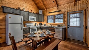 A wooden cabin kitchen with a dining table set for four, a refrigerator, microwave, and a sink. - 8 Miles to Pigeon Forge, 15 Miles to Gatlinburg, Sleeps 8, Pool Table, Hot Tub, Game Room (Sevierville)
