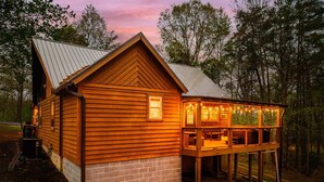 A wooden cabin with a brick foundation, a porch with string lights, and a metal roof. - 8 Miles to Pigeon Forge, 15 Miles to Gatlinburg, Sleeps 8, Pool Table, Hot Tub, Game Room (Sevierville)