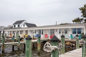 A waterfront property with a dock, a white building with multiple windows, and outdoor seating with colorful chairs.