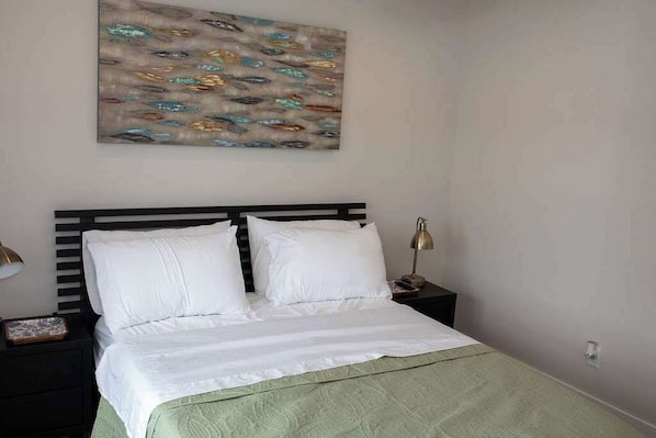 A neatly made bed with white linens and a green blanket, a black headboard, and a bedside table with a lamp.