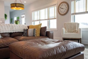 A modern living room with a leather sectional sofa, a white armchair, and a large wall clock.
