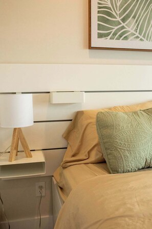 Une chambre à coucher avec un lit, une table de chevet, une lampe et une œuvre d’art encadrée accrochée au mur.