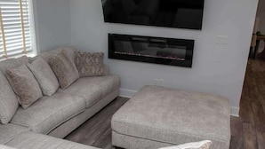 Un salon comprenant un canapé d’angle, un pouf et un téléviseur à écran plat fixé au mur.
