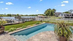 Une piscine avec une terrasse en bois, une clôture blanche en piquets et une vue sur un lac.