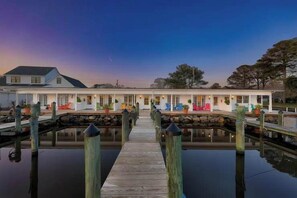 A waterfront hotel with a wooden dock leading to a row of rooms, each with a balcony and potted plants.