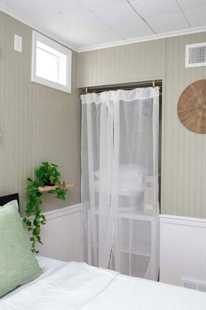Une chambre à coucher avec un lit, une fenêtre ornée d’un rideau léger, une plante fixée au mur et un élément décoratif texturé sur le mur.