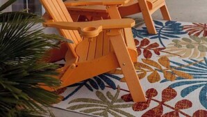 Une véranda couverte avec deux fauteuils Adirondack en bois et une petite table, un tapis à motifs et une plante en pot.