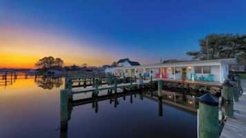 A waterfront property with a dock extending into calm water, a covered walkway, and a building with multiple windows.