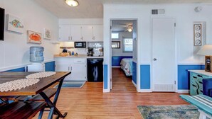 A compact kitchen with white cabinets, a microwave, and a water dispenser. A dining table with a placemat is in the foreground.
