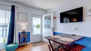 Un comedor con una mesa de madera, sillas, un televisor montado en la pared y un ventanal con cortinas.