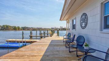 A wooden dock extending into a calm body of water, with a building on the right featuring a circular emblem and outdoor seating.
