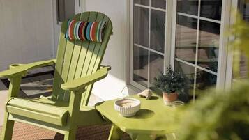 Una silla Adirondack verde con cojín, una mesita con un cuenco y una planta en maceta.