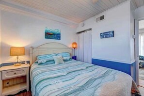 A bedroom with a bed, nightstand, lamp, and a sign indicating the direction to the beach.