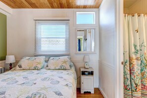 Una camera da letto con un letto, un comodino, una finestra con persiane, uno specchio e una porta con tende.