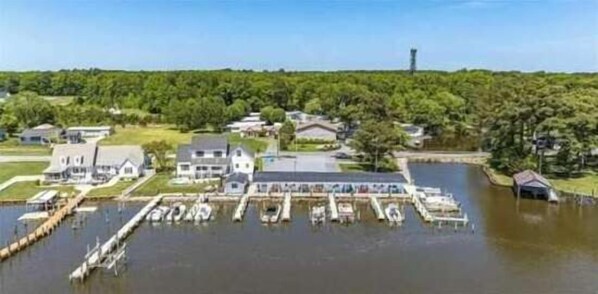 A marina with several boats docked, surrounded by residential houses and a forested area in the background.