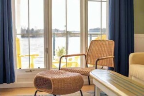 A room with a large window, wicker chairs, a bench, and a view of a body of water.