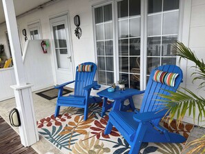 Eine Veranda mit zwei blauen Adirondack-Stühlen, einem kleinen Tisch und einem Zierteppich.