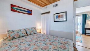 A bedroom with a floral bedspread, a ceiling fan, a framed picture, and a door leading to another room.
