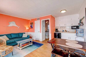 A living room with a teal sofa, a wooden coffee table, and a dining table with a placemat. There is a kitchen area with white cabinets and a microwave. - Inn on Turville Cottage, Sleeps 4, Waterfront (Berlin)