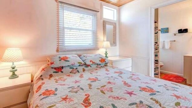 Ein Schlafzimmer mit einem Bett, zwei Nachttischen, einem Fenster mit Jalousien, einem Spiegel und einer Tür mit Schuhablage.