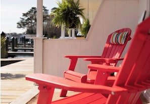 A wooden deck with red Adirondack chairs and a potted plant.