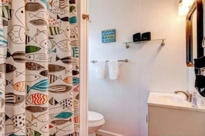 A bathroom with a toilet, a sink, a mirror, and a shower curtain with a fish pattern.