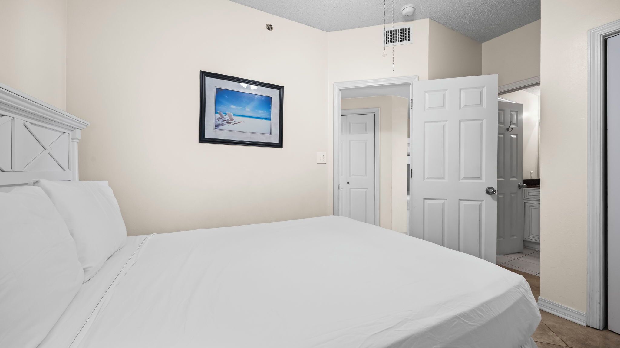 A bedroom with a bed, a framed picture on the wall, and a door leading to another room.