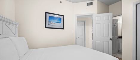 A bedroom with a bed, a framed picture on the wall, and a door leading to another room.