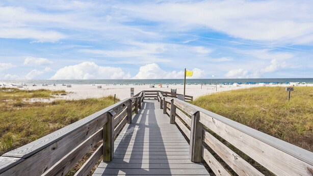 A wooden boardwalk leading to a beach with a flag marking the start of the dunes. - Gulf front condo w/ pools, gym, hot tub, sauna & beach path! (Orange Beach)