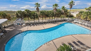A pool with clear blue water, surrounded by lounge chairs and palm trees, with a view of the beach and ocean in the background. - Gulf front condo w/ pools, gym, hot tub, sauna & beach path! (Orange Beach)