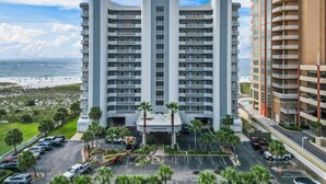 A multi-story hotel with a central entrance, parking lot, and a view of the beach. - Gulf front condo w/ pools, gym, hot tub, sauna & beach path! (Orange Beach)