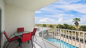 Ein Balkon mit einem Glastisch und roten Stühlen mit Blick auf einen Swimmingpool und einen Strand.